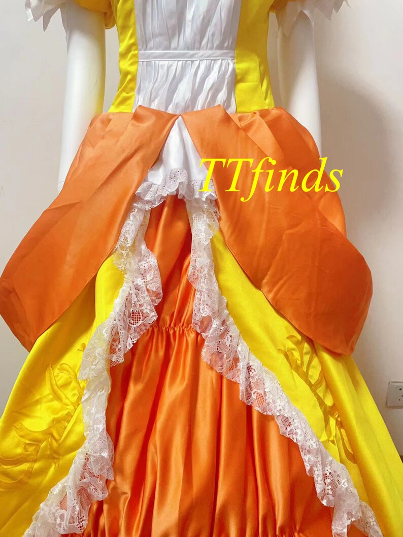 May include: A yellow and orange dress with white lace trim and a white bodice. The dress has a large bow in the back and is made of a satin-like fabric. The dress is a vintage style and is perfect for a special occasion.