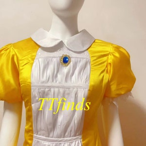May include: A yellow and orange dress with a white bodice and a blue gem brooch. The dress has a Peter Pan collar and short sleeves. The text "TTfinds" is visible on the dress.