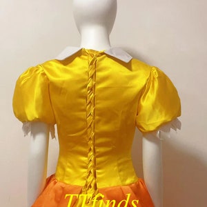 May include: A yellow and orange dress with a white collar and puff sleeves. The dress has a lace-up back and a full skirt.