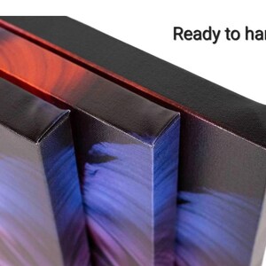 Pu&ograve; includere: Tre stampe su tela rettangolari con bordi avvolti che presentano sfumature di colore rosso, viola e blu. I bordi laterali sono neri e il testo Ready to hang &egrave; stampato in nero nell'angolo in alto a destra dell'immagine.