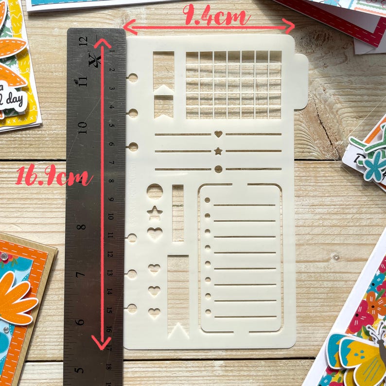 Może przedstawiać: Biała plastikowa szablon z siatką, liniami, sercami, gwiazdami i k&oacute;łkami. Szablon ma 9,4 cm szerokości i 16 cm wysokości.