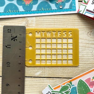 Op de afbeelding: Een geel plastic raster met de dagen van de week gelabeld "MTWTFSS" bovenaan. Het raster heeft 7 kolommen en 6 rijen.