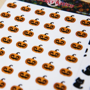 Peut inclure: Une feuille d'autocollants d'Halloween avec plusieurs visages de citrouille orange avec des yeux et des bouches noirs. Les autocollants sont sur un fond blanc avec le texte "Sticker Kitten" et "Halloween Stickers" imprim&eacute; sur la feuille.
