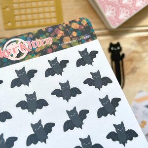 May include: A sheet of Halloween stickers featuring 16 black bats with white eyes and smiles. The stickers are on a white background with a colourful design and the text "Sticker Kitten Halloween stickers".
