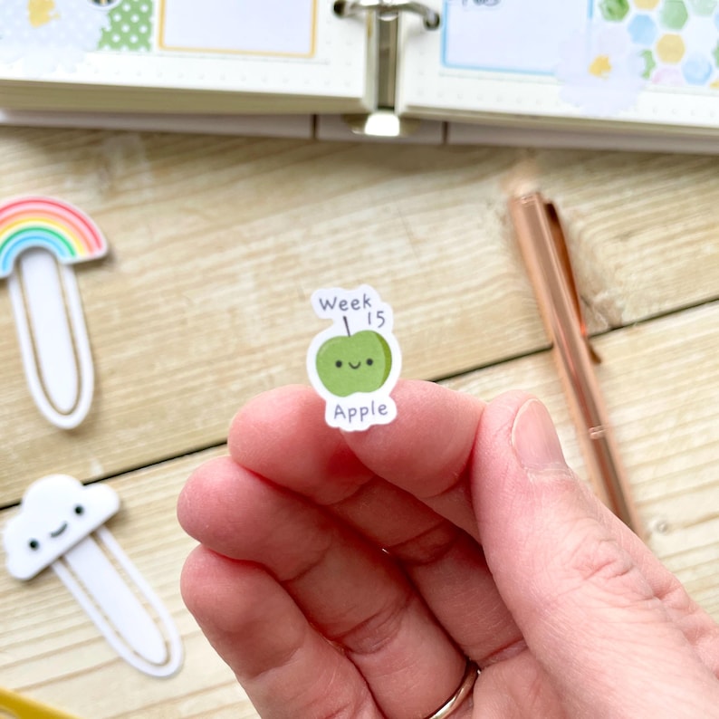Puede incluir: Una pegatina de manzana verde con una cara sonriente y el texto "Week 15" arriba y "Apple" abajo.