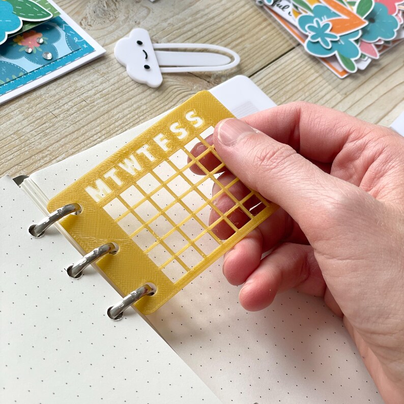 Op de afbeelding: Een geel plastic raster met de dagen van de week met de label "MTWTFSS" wordt gebruikt om dagen in een planner af te vinken.