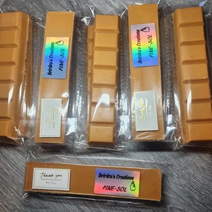 May include: Six bars of brown wax melt with a label that says "Deirdra's Creations PINE-SOL". The wax melts are individually wrapped in clear plastic.