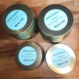 May include: Four gold-colored metal tins with light blue labels. Each label reads "Deirdra's Creations," "8 ounces," "Made from coconut apricot wax," and "Motor Oil."