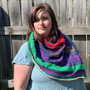 May include: A person wearing a teal blue shirt with a colourful crocheted shawl. The shawl has a variety of colours including red, purple, green, and pink.