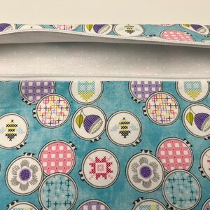 Pu&ograve; includere: Una pochette con cerniera turchese con una fodera a pois bianchi. La pochette &egrave; decorata con un motivo ripetitivo di cerchi bianchi che contengono disegni di ricamo colorati.