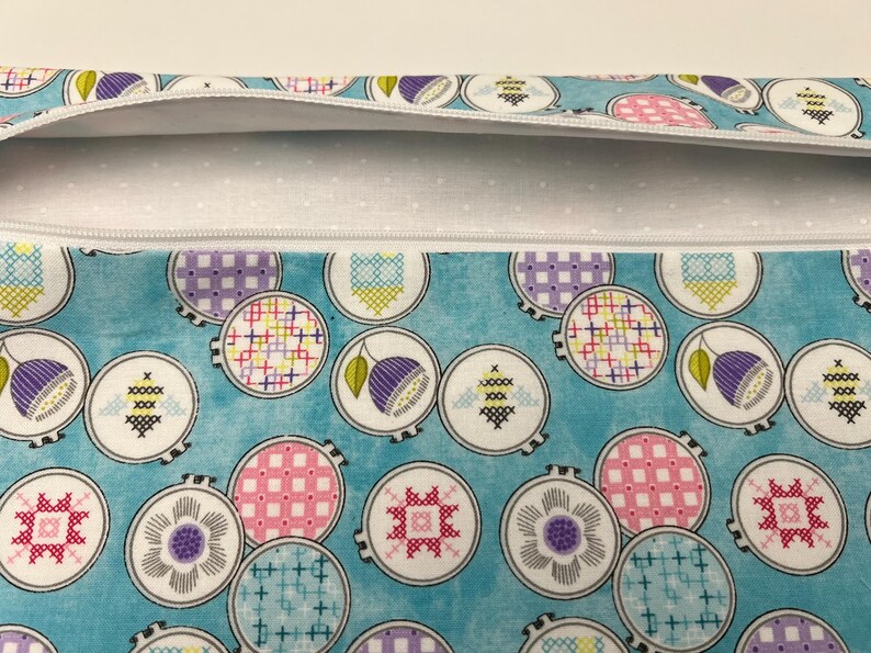 Pu&ograve; includere: Una pochette con cerniera turchese con una fodera a pois bianchi. La pochette &egrave; decorata con un motivo ripetitivo di cerchi bianchi che contengono disegni di ricamo colorati.