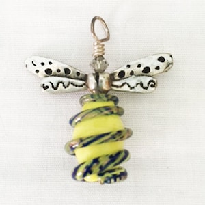 Peut inclure: Pendentif libellule artisanal avec un corps en verre jaune et bleu et des ailes argentées. Les ailes ont des pois noirs. Le pendentif a une boucle en fil d'argent pour l'accrochage. Le pendentif libellule est un bijou unique.