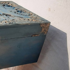 May include: A blue wooden box with intricate carvings on the top. The box has gold metal accents on the corners.