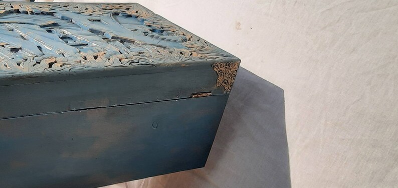 May include: A blue wooden box with intricate carvings on the top. The box has gold metal accents on the corners.