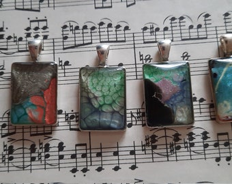 May include: Four silver rectangular pendants with colorful abstract resin art. Each pendant features a unique design with swirling colors and patterns.