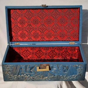 May include: A blue wooden box with a red patterned lining and a carved design of ships on the front. The box has a brass latch.