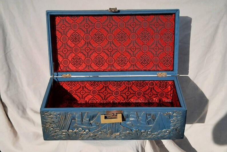 May include: A blue wooden box with a red patterned lining and a carved design of ships on the front. The box has a brass latch.