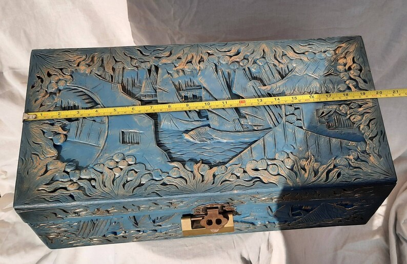 May include: A blue wooden chest with intricate carvings of a Chinese landscape scene. The chest has a brass lock and hinges. The chest is approximately 19 inches long.