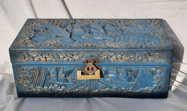May include: A blue wooden chest with intricate carvings of ships and floral designs. The chest has a brass latch and a wooden handle.