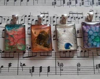 May include: Four rectangular silver pendants with colorful resin inserts. The pendants feature abstract designs in shades of pink, orange, brown, blue, purple, and green.
