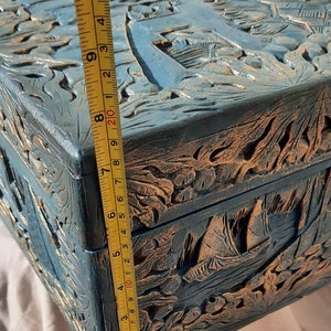 May include: A wooden box with intricate carvings of a seascape. The box is painted in shades of blue and gold, and measures approximately 8 inches in length.