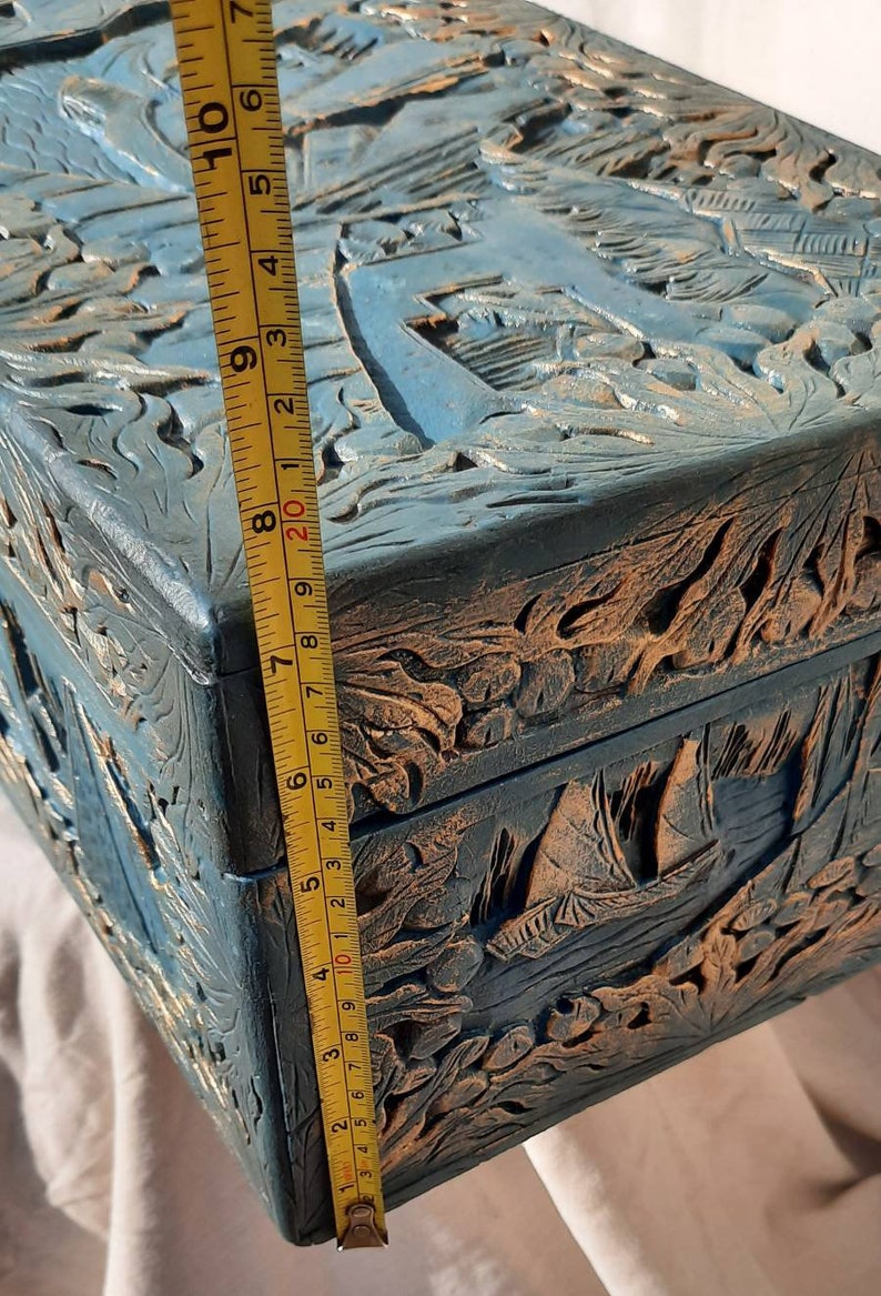 May include: A wooden box with intricate carvings of a seascape. The box is painted in shades of blue and gold, and measures approximately 8 inches in length.