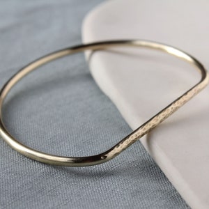 May include: A gold hammered bangle bracelet. The bracelet is made of thick, rounded metal and has a hammered texture.