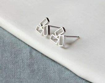 May include: A pair of silver geometric stud earrings with a minimalist design. The earrings are made of multiple overlapping rectangles.