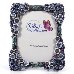 May include: A decorative photo frame with a floral design. The frame is adorned with blue and purple flowers and has a teal-colored border. The text "J.B.S. Collection" and "Novelty hand painted frames" are visible. A butterfly graphic is also present.
