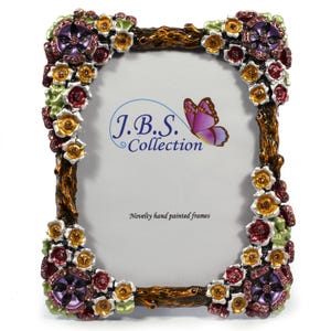 May include: Ornate photo frame with a floral design. The frame is brown with colorful flowers in shades of purple, red, yellow, and green. The text "J.B.S. Collection" and "Novelty hand painted frames" are visible.