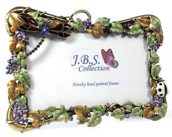 May include: Ornate, hand-painted photo frame with a dragonfly, grapes, and leaves design. The frame is gold-toned with green, brown, and purple accents. The text on the frame reads "J.B.S. Collection" and "Novelty hand painted frames".