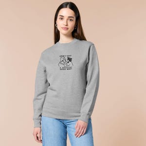 An embroidered light grey sweater design of the Australian Jack Karlson being arrested while he shouts Eating A Meal? A Succulent Chinese Meal?!