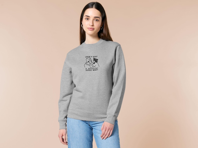 An embroidered light grey sweater design of the Australian Jack Karlson being arrested while he shouts Eating A Meal? A Succulent Chinese Meal?!