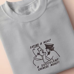An embroidered light grey t-shirt design of the Australian Jack Karlson being arrested while he shouts Eating A Meal? A Succulent Chinese Meal?!
