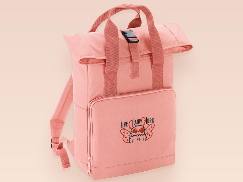 Pink roll top backpack with a front pocket and an embroided mothman cryptid design with the lext live lamp lurk