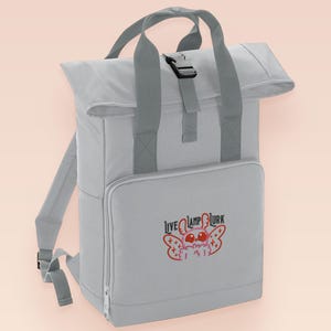 Grey roll top backpack with a front pocket and an embroided mothman cryptid design with the lext live lamp lurk