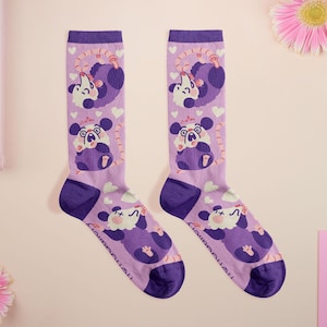May include: Two pairs of knee-high socks with a purple and white possum design. The socks are lavender with purple accents at the toe, heel, and cuff. The possum illustrations are in various poses, with hearts and clouds scattered across the socks.