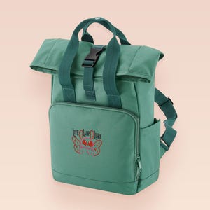 Green roll top backpack with a front pocket and an embroided mothman cryptid design with the lext live lamp lurk