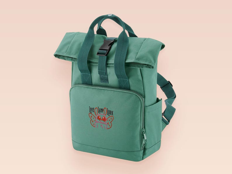 Green roll top backpack with a front pocket and an embroided mothman cryptid design with the lext live lamp lurk