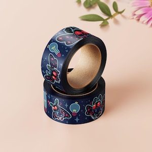 Op de afbeelding: Twee rollen washi tape met een donkerblauwe achtergrond en een herhalend patroon van motten en gloeilampen. De motten zijn roze en zwart met gloeiende ogen. De gloeilampen zijn geel en wit.