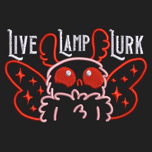 May include: Embroidered design on a black background featuring the text "LIVE LAMP LURK" above a cartoon moth-like creature with red eyes and wings. The design includes red and white thread.