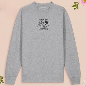 An embroidered light grey sweater design of the Australian Jack Karlson being arrested while he shouts Eating A Meal? A Succulent Chinese Meal?!