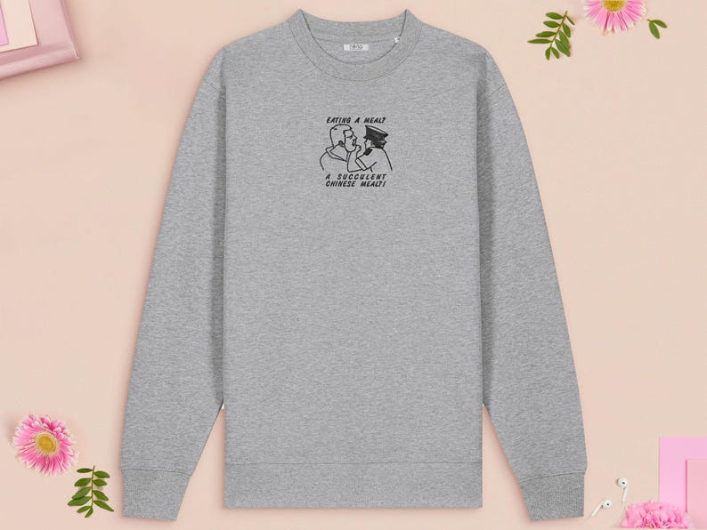 An embroidered light grey sweater design of the Australian Jack Karlson being arrested while he shouts Eating A Meal? A Succulent Chinese Meal?!