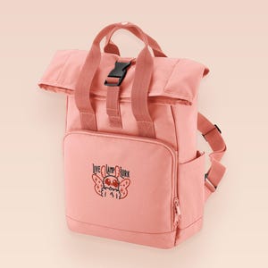 Pink roll top backpack with a front pocket and an embroided mothman cryptid design with the lext live lamp lurk