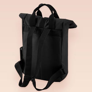 Black roll top backpack with a front pocket and an embroided mothman cryptid design with the lext live lamp lurk