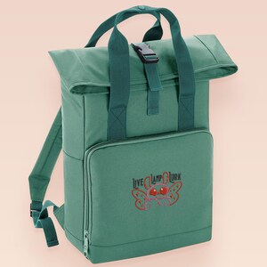 Green roll top backpack with a front pocket and an embroided mothman cryptid design with the lext live lamp lurk