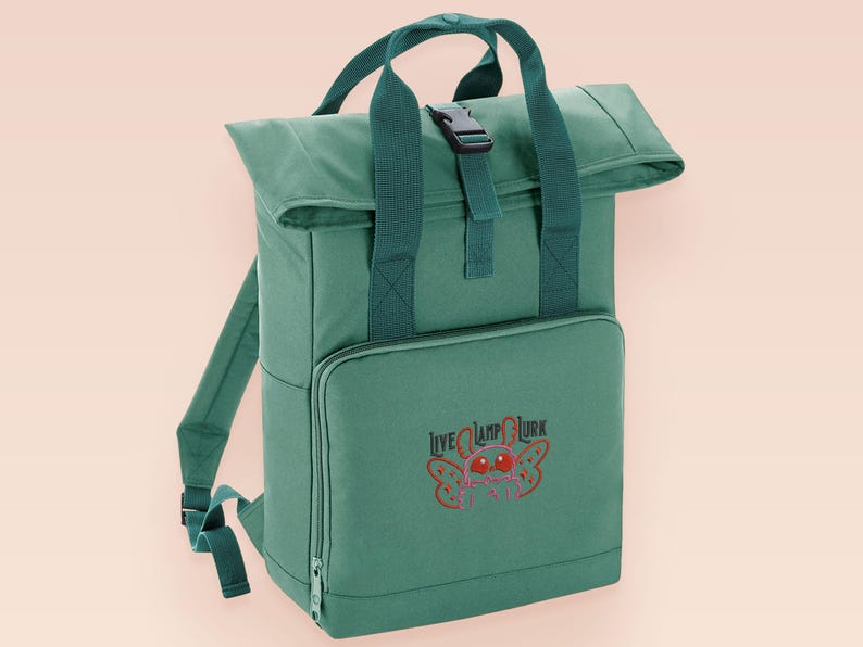 Green roll top backpack with a front pocket and an embroided mothman cryptid design with the lext live lamp lurk