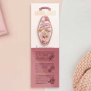 May include: Pink and gold enamel pin with a motel key design. The pin features the text "Animal Lover's Talisman" and floral accents. The pin is on a white card with text about inspiring a love for nature, caring for animals, and the conservationist's stone.