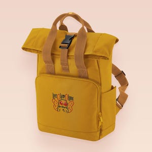 Yellow roll top backpack with a front pocket and an embroided mothman cryptid design with the lext live lamp lurk