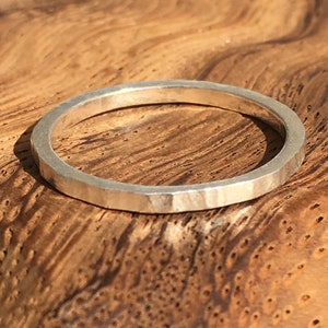 Op de afbeelding: Een gehammerde zilveren ring op een houten oppervlak. De ring is een eenvoudige band met een getextureerde afwerking. De tekst "Hammered Thread Ring" is zichtbaar onder de ring.